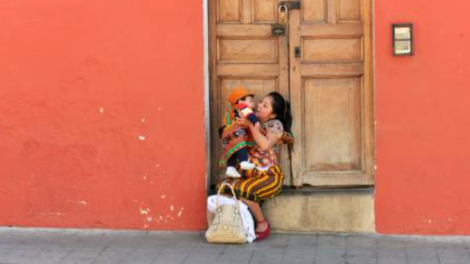 straatbeeld in Guatemala, moeder zit met kind op de stoep voor een oranje huis